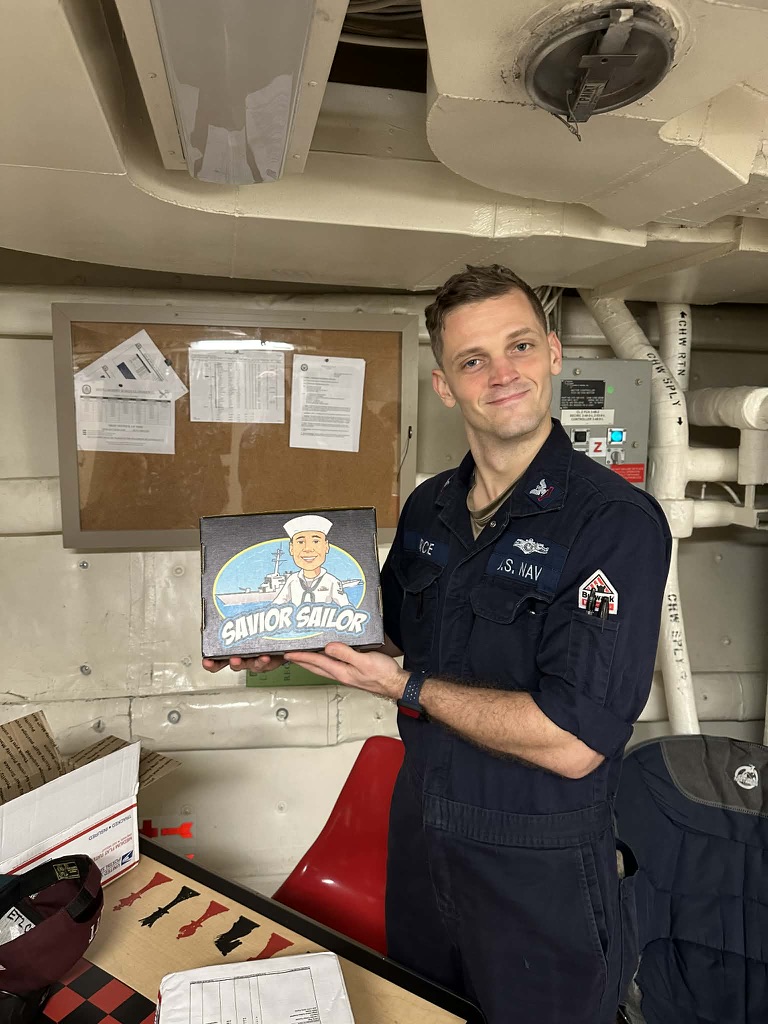 Navy petty officer displaying his Savior Sailor care package in a shipboard workspace