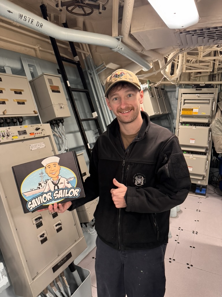 Sailor in a fleece jacket holding his Savior Sailor care package with a thumbs up